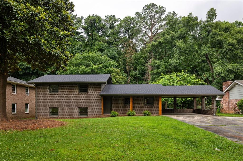Two-story brick house with a long covered carport and wooded backdrop.
