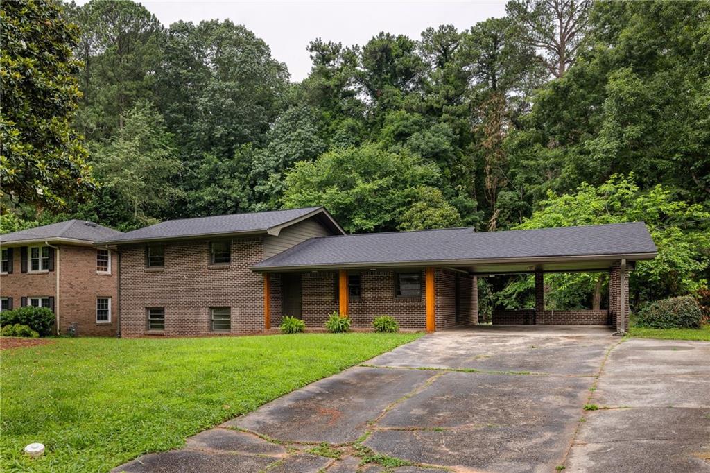 Brick home with a wide covered carport and driveway, set among mature trees.