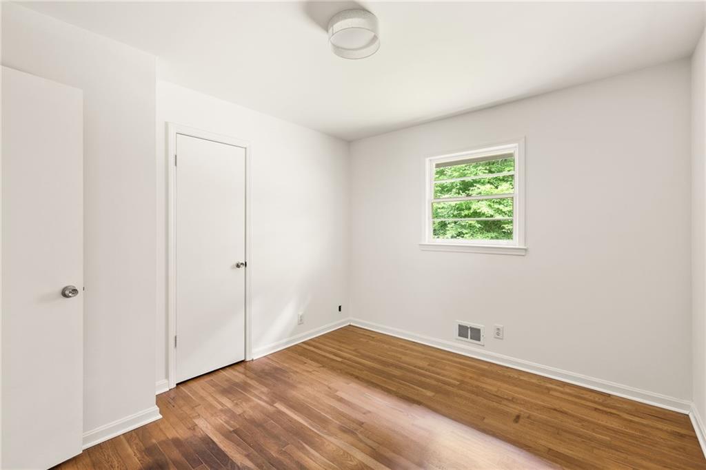 Empty room with hardwood floors, white walls, and a window overlooking greenery.