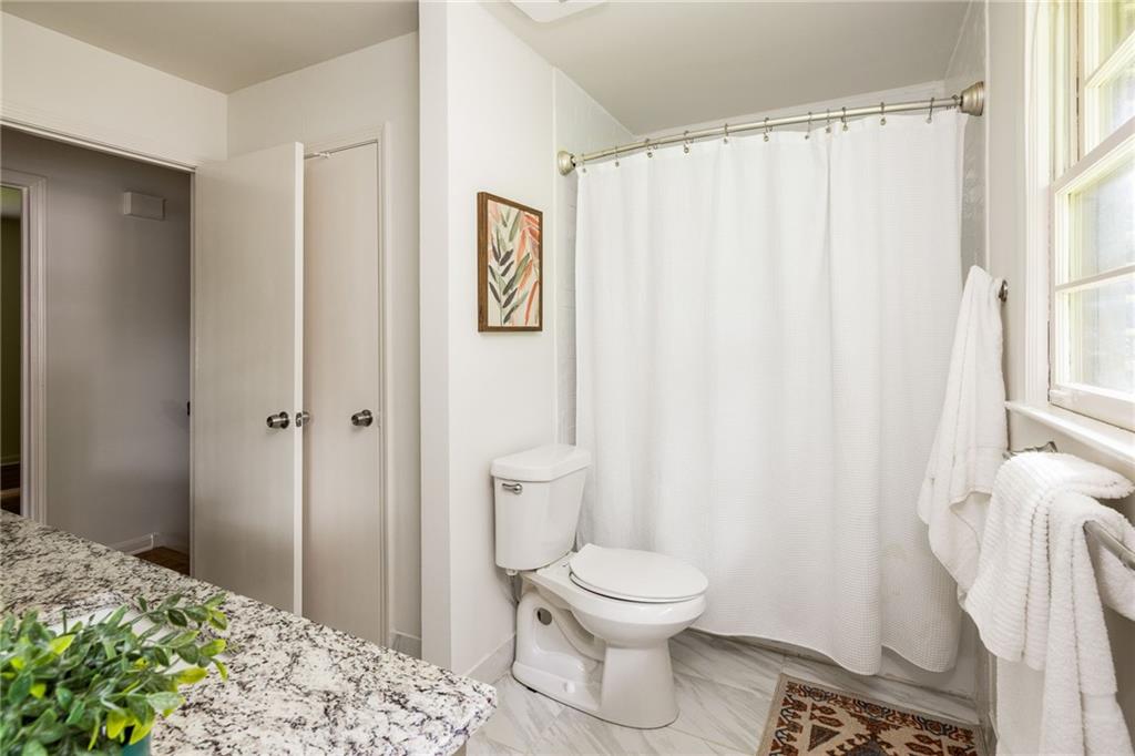 Bathroom with a white shower curtain, marble-patterned vanity, and bright window.