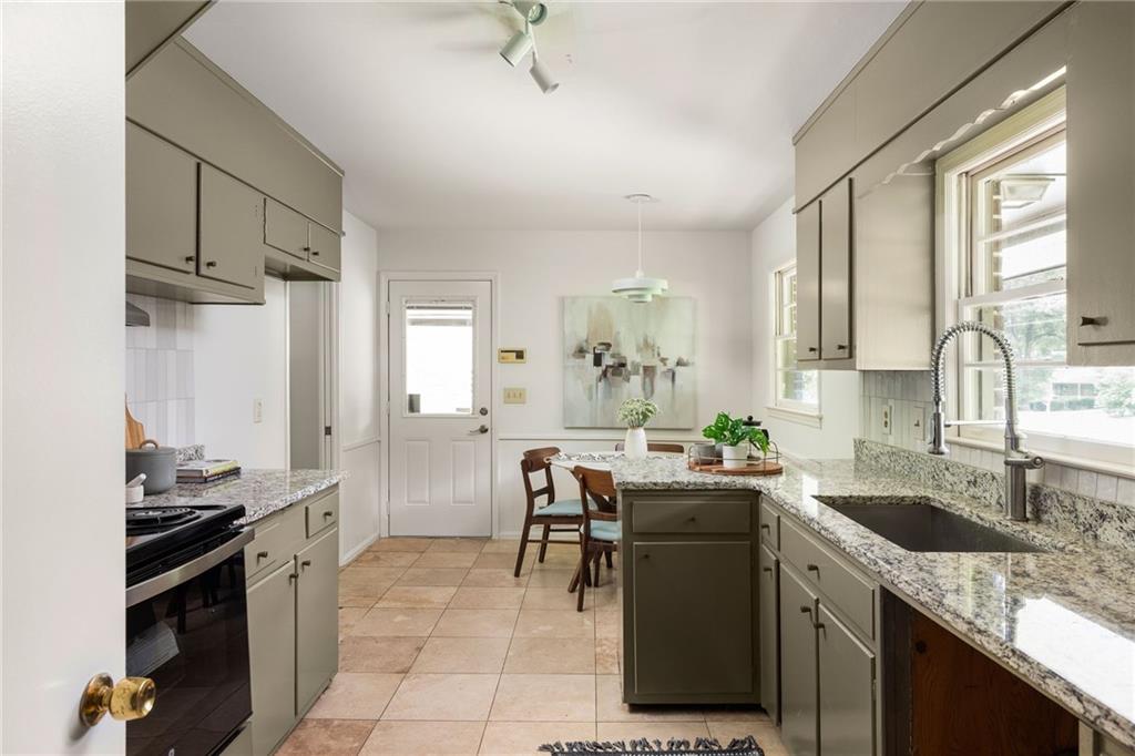 Kitchen with gray cabinets, granite counters, a deep sink beneath windows, and a dining table.