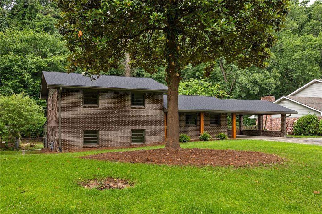 Brick split-level home with a long carport, broad lawn, and large shade tree.