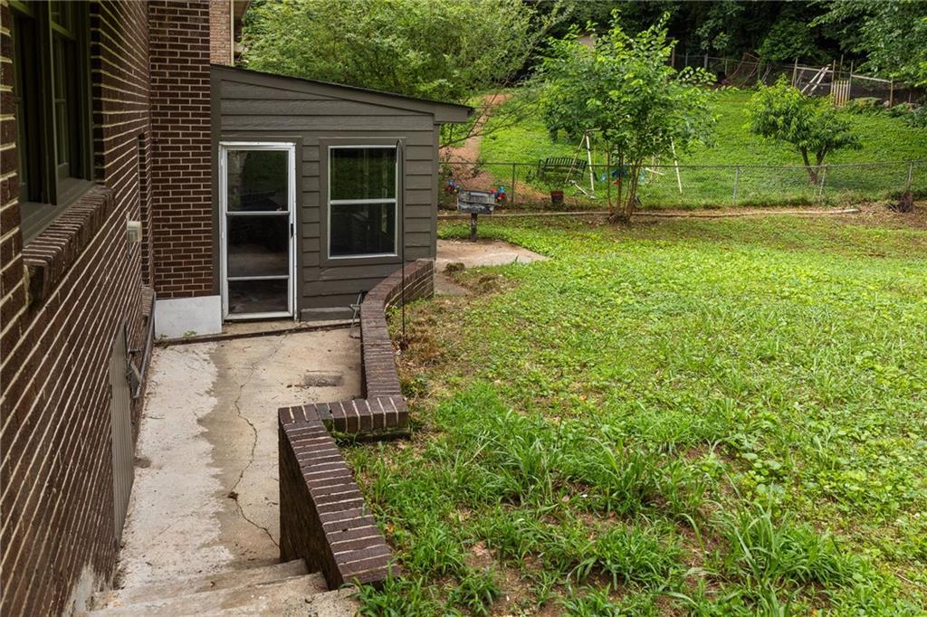 Side yard beside a brick home, with a concrete walkway, fenced lawn, and play set.