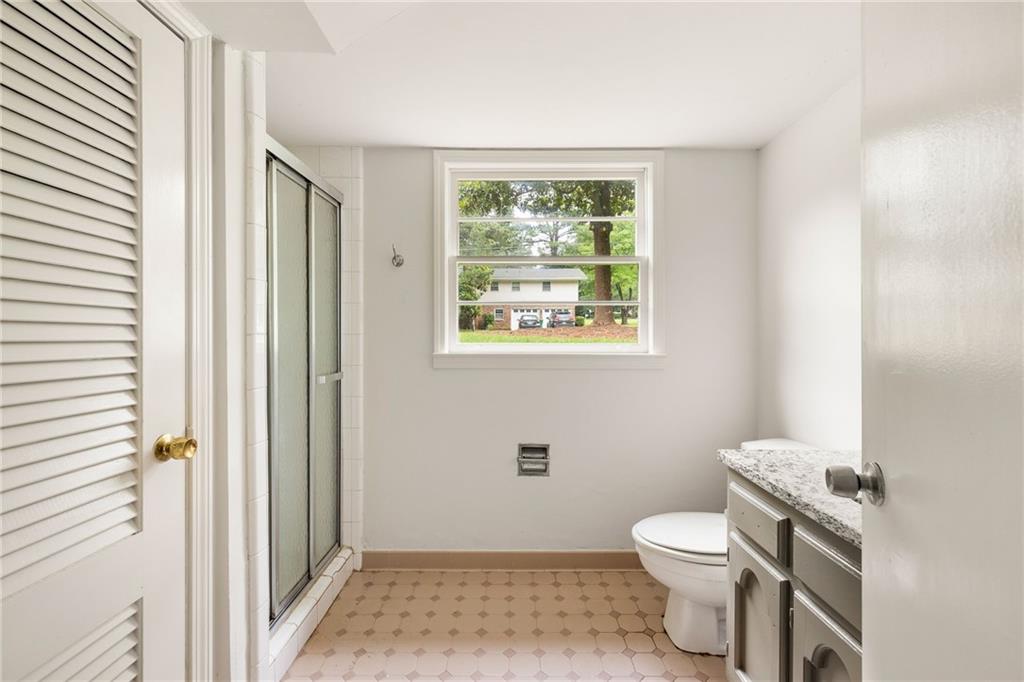 Bathroom with glass shower, stone-countertop vanity, patterned tile floor, and a window overlooking trees.