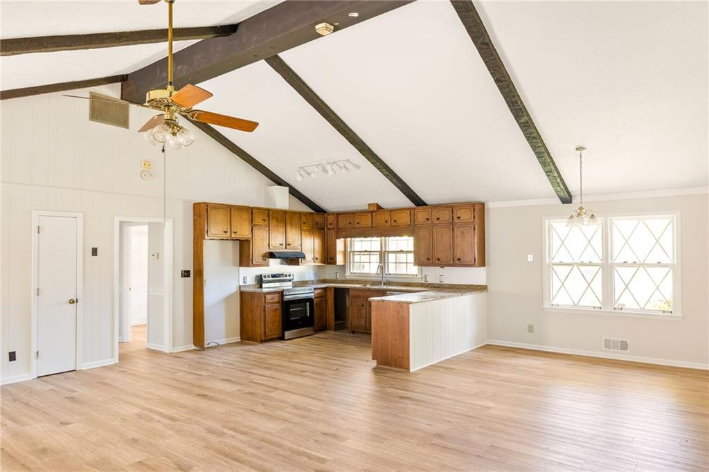 Vacant kitchen with wood cabinets and peninsula beneath a vaulted ceiling with exposed beams.