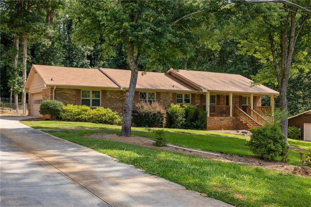 Brick ranch home with an attached garage and covered porch, surrounded by mature trees.