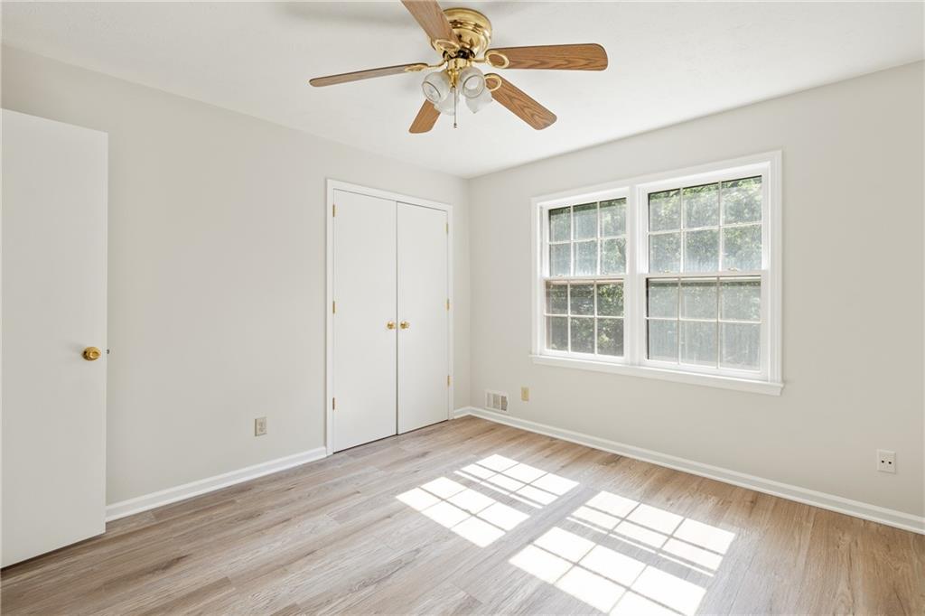 Empty bedroom with wood flooring, a ceiling fan, and a large window.