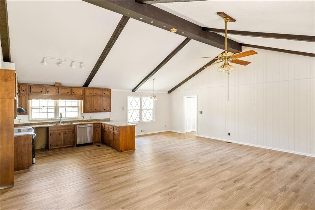 Open kitchen and living area with wood cabinets, light flooring, and exposed ceiling beams.