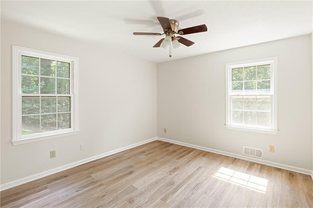 Empty room with light wood-look floors, two windows, and a ceiling fan.