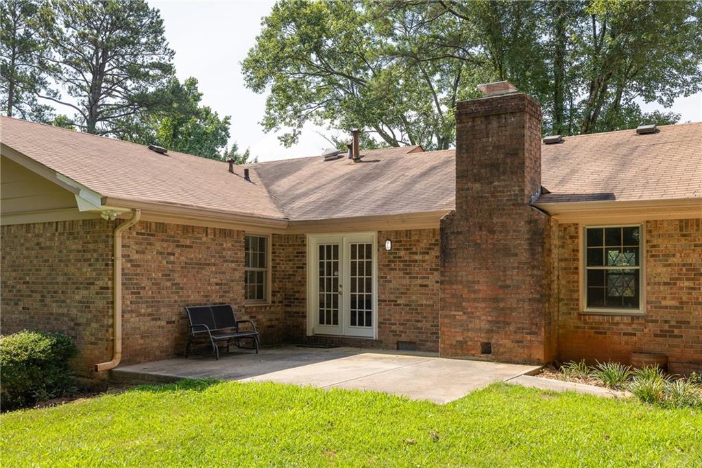 Brick rear of the home with a concrete patio, French doors, and a large chimney.