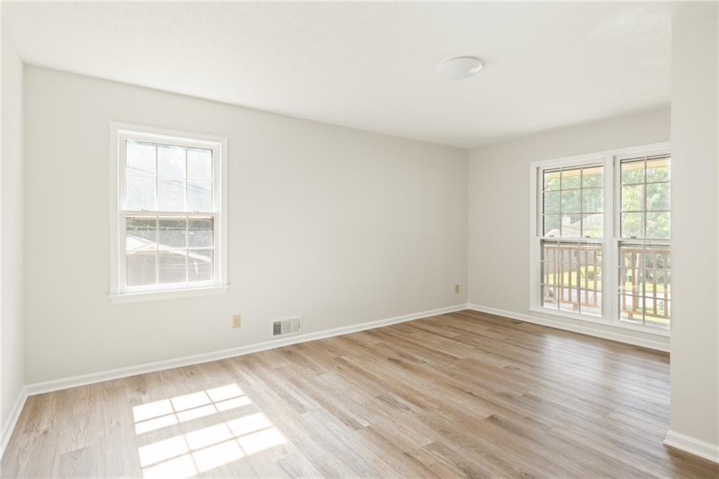 Empty room with light wood-look floors and windows overlooking a deck.