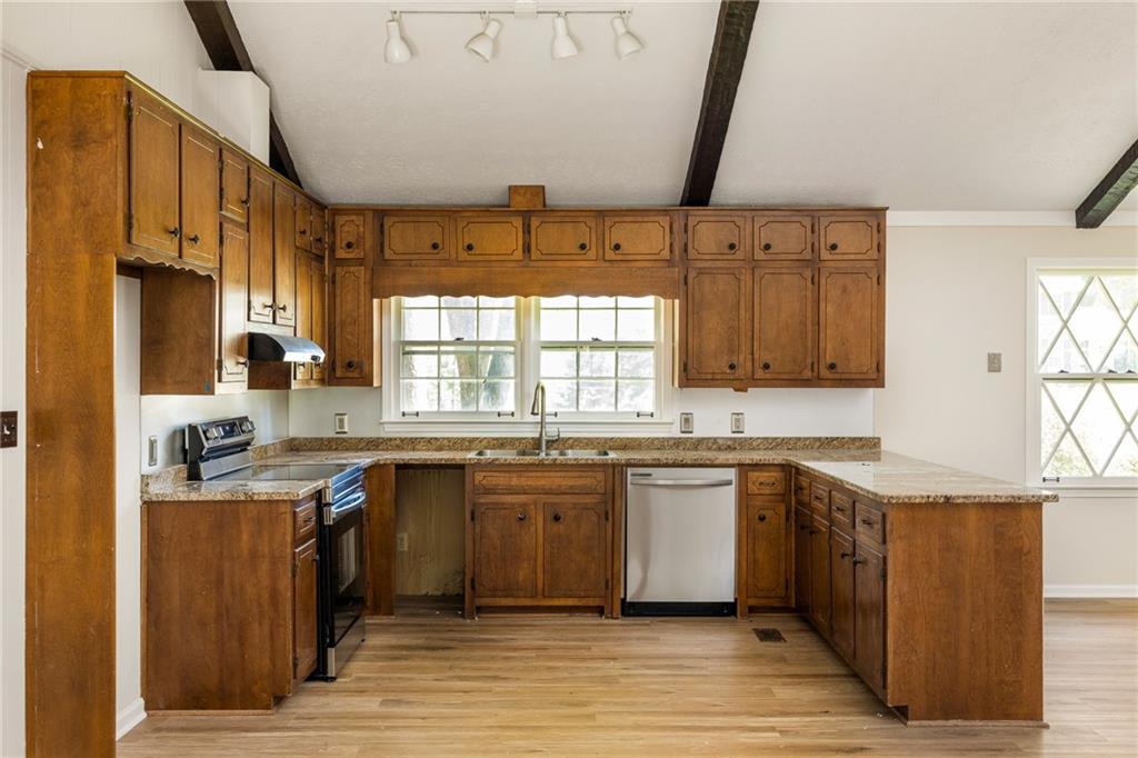 Kitchen with honey-brown cabinets, granite counters, a double window above the sink, and light wood flooring.