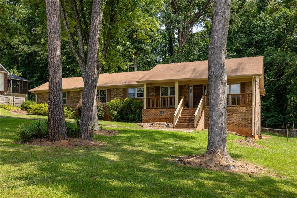 Brick ranch home with a raised front porch, framed by mature trees and a grassy lawn.