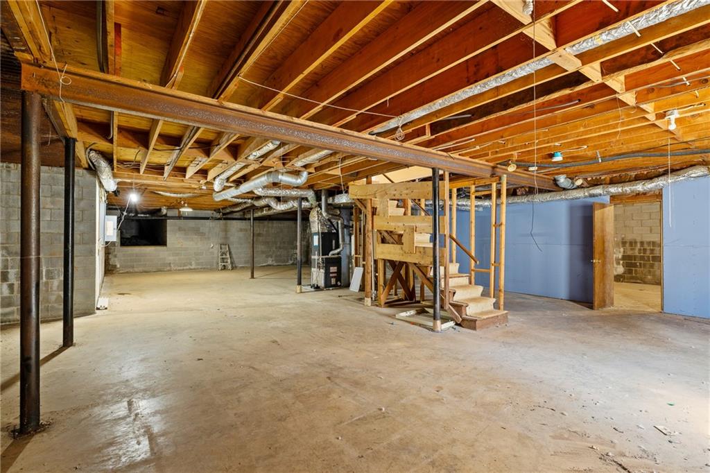 Unfinished basement with exposed ceiling joists, visible ductwork, and stairs.