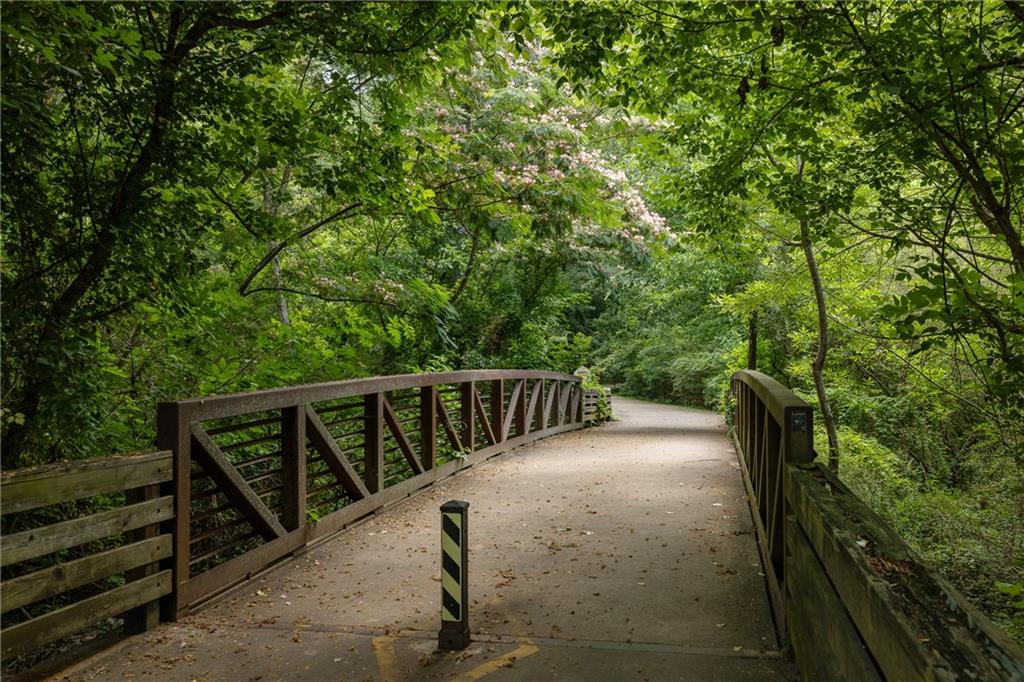 Pedestrian bridge curving through dense green woodland, with dark metal railings.
