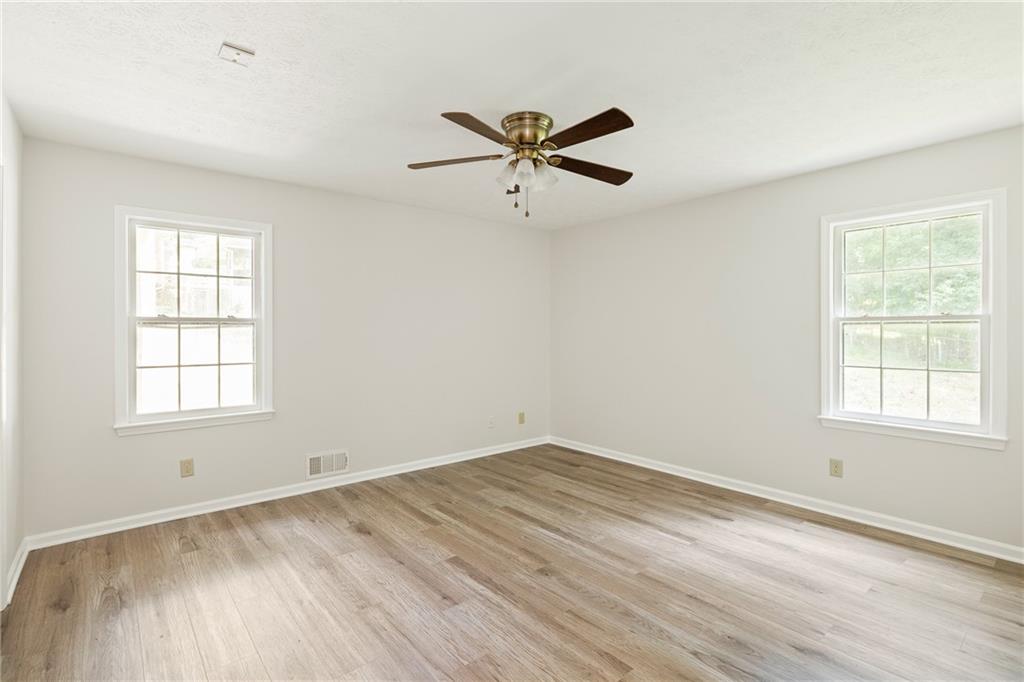 Empty bedroom with wood-look flooring, two windows, and a ceiling fan.