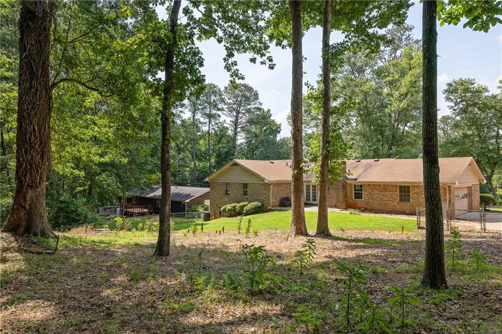 Brick ranch house on a wooded lot, seen through tall trees beside a detached outbuilding.