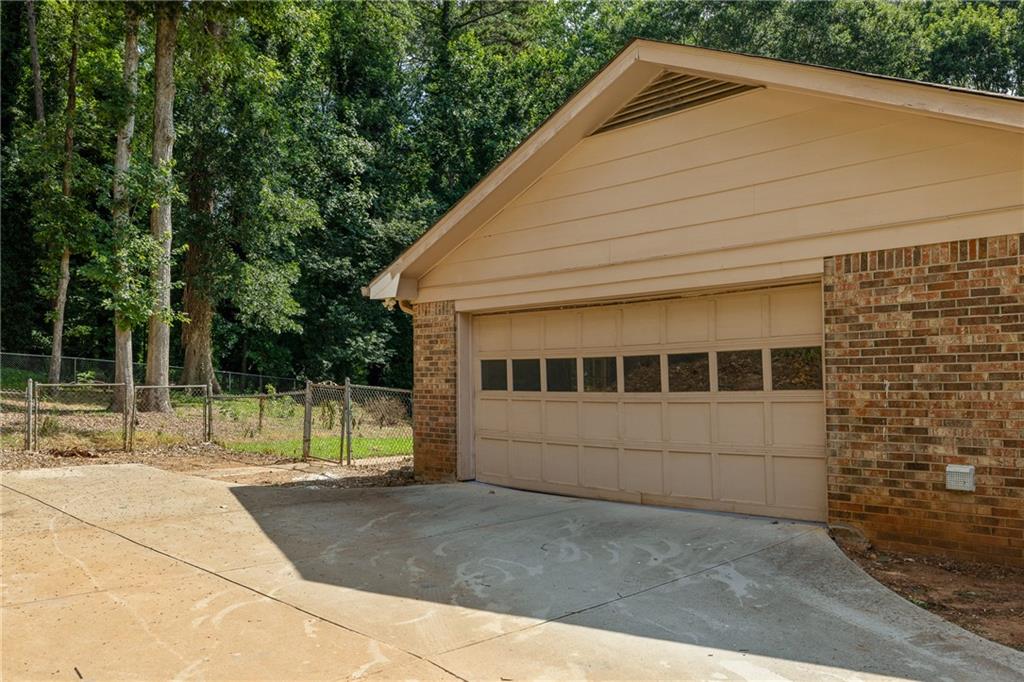 Attached brick garage with a tan gable and wide concrete driveway beside a fenced, wooded yard.