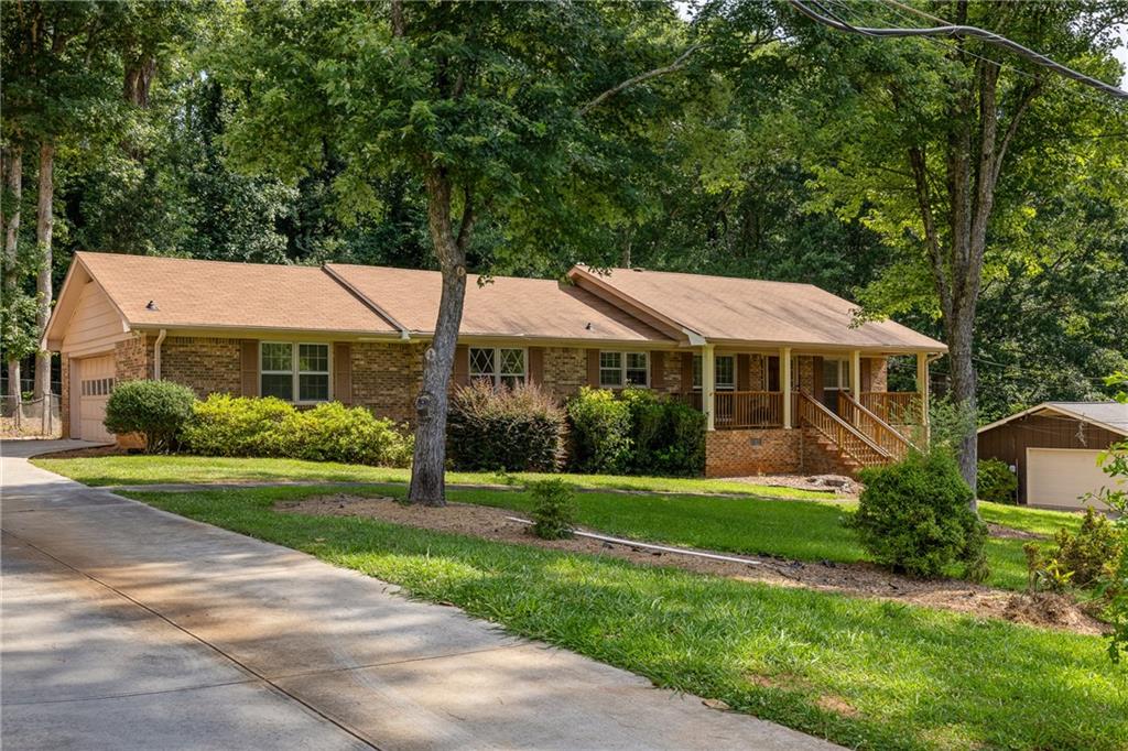 Single-story brick home with a covered porch, driveway, and mature trees.