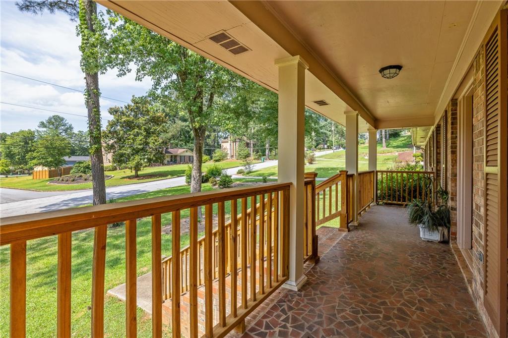 Covered front porch with flagstone flooring and wooden railings overlooking a leafy street.