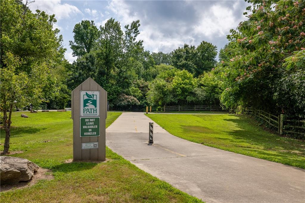 Paved community trail entrance with a PATH sign, lawns, mature trees, and wooden fencing.