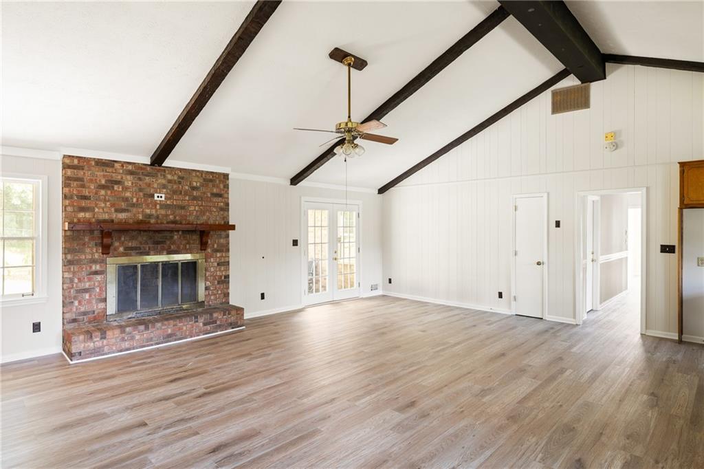 Empty living room with a brick fireplace, vaulted ceiling, exposed beams, and French doors.