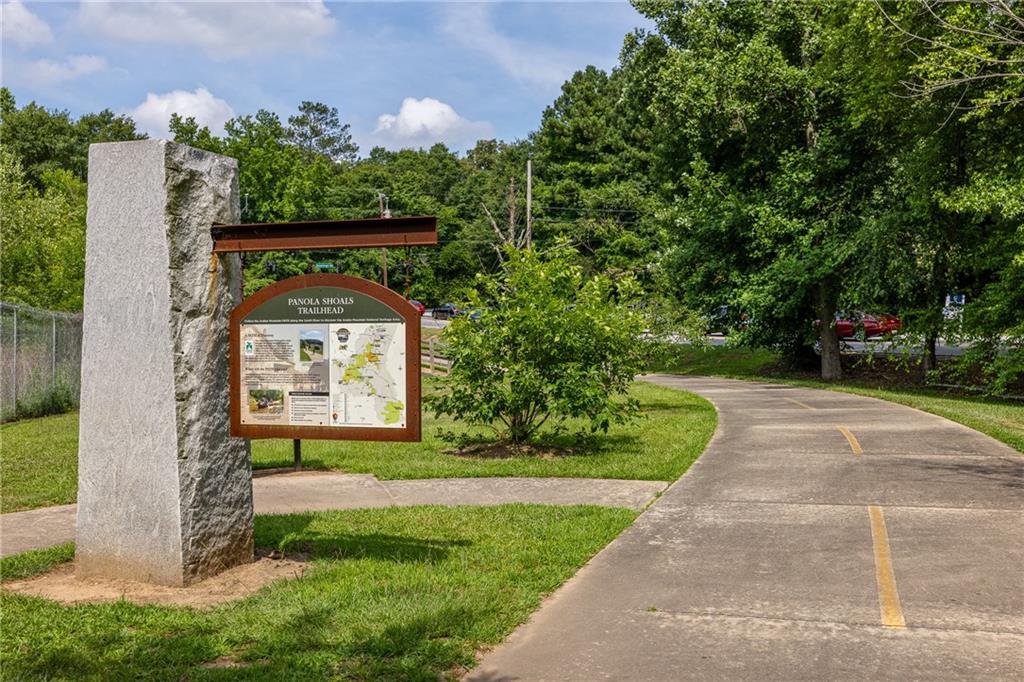 Panola Shoals Trailhead sign beside a paved path curving through a leafy park.