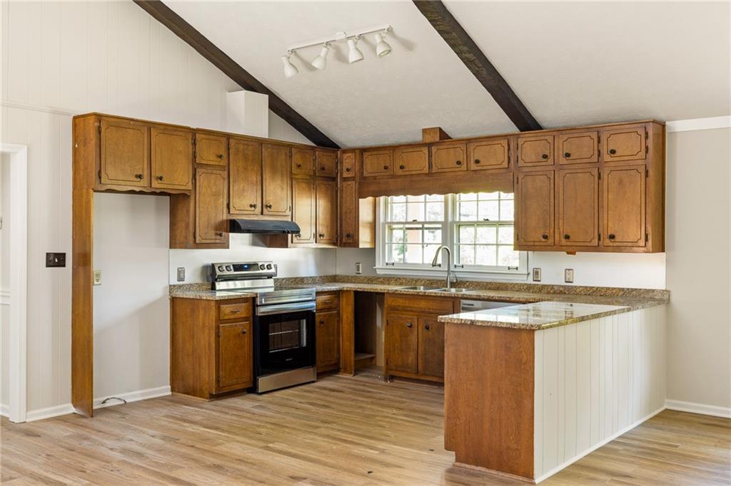 Kitchen with extensive wood cabinetry, granite island, stainless steel range, and exposed ceiling beams.