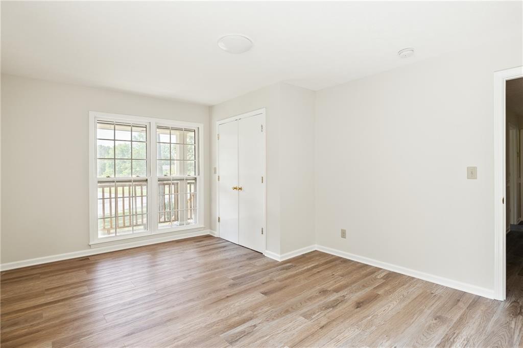 Empty room with wood-look floors, paired deck-facing windows, and double closet doors.