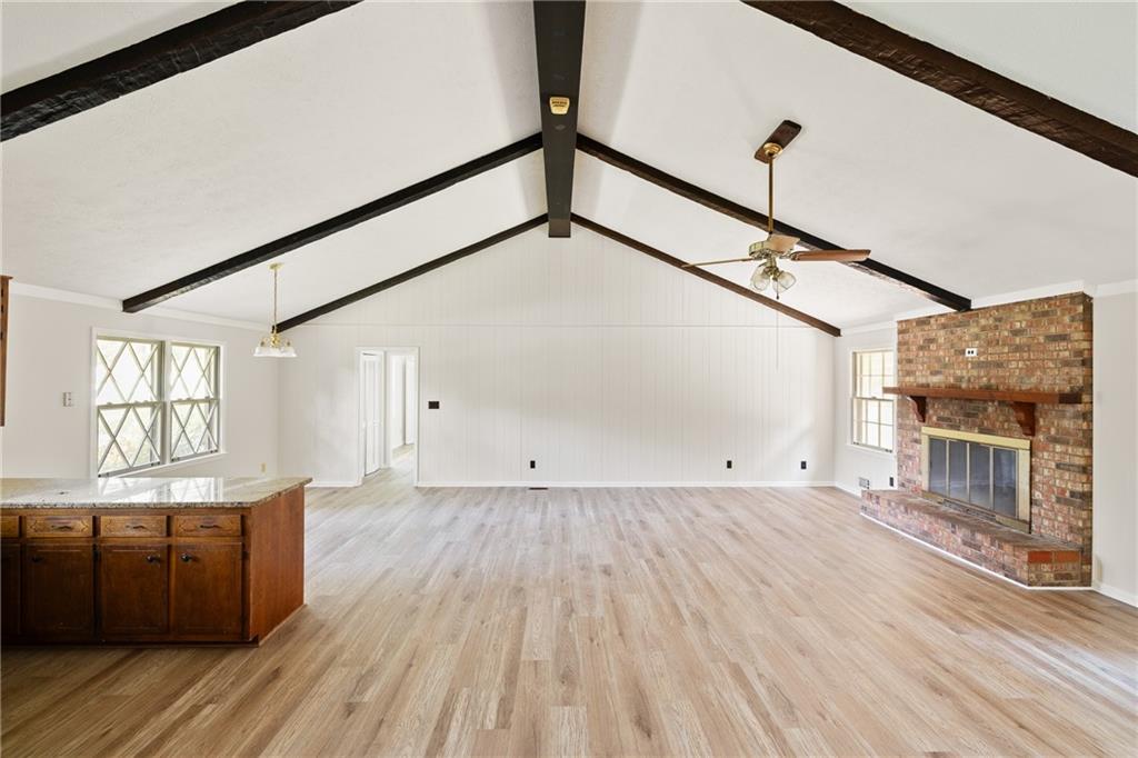 Vacant living room with vaulted beam ceiling, brick fireplace, and light wood flooring.