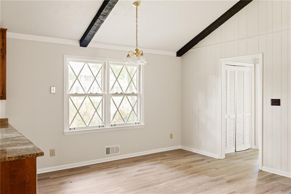 Empty dining area with exposed ceiling beams, diamond-pane windows, and louvered doors.