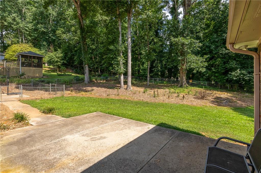 Backyard patio and lawn bordered by mature trees, with a gazebo and chain-link fence.