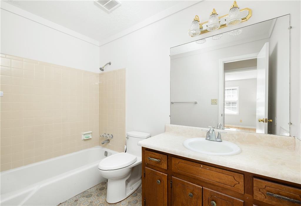 Bathroom with beige tub surround, white bathtub, and wood vanity beneath a large mirror.