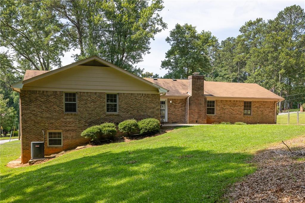 Brick home’s rear and side exterior with a chimney, sloping lawn, and mature trees.