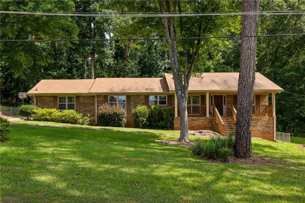 Brick ranch home with a covered porch, broad lawn, and mature trees.