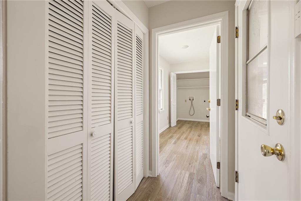 Hallway leading to a laundry area with hookups, shelving, and louvered closet doors.