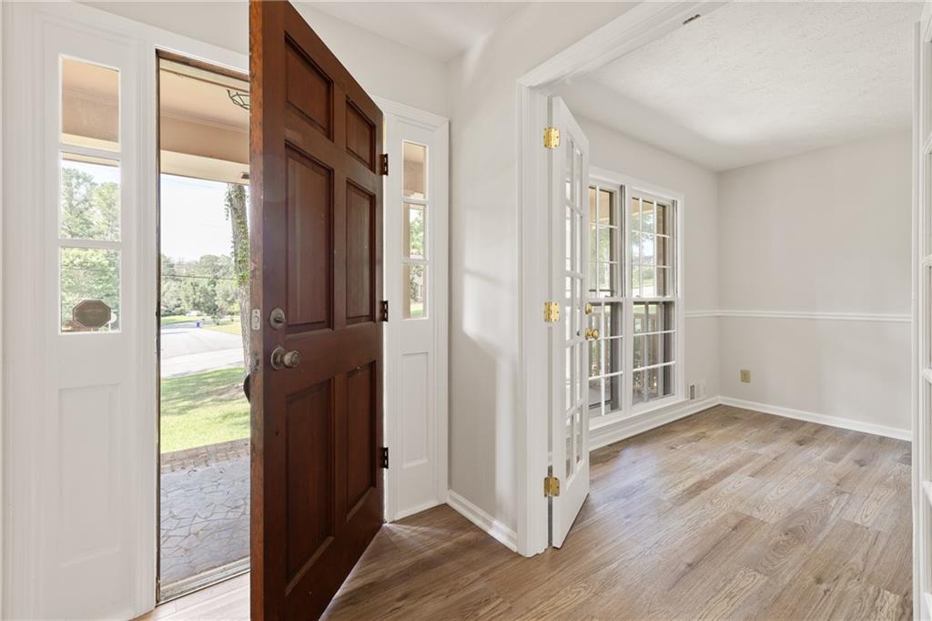 Entryway with an open dark wood front door and white French doors beside wood-look flooring.