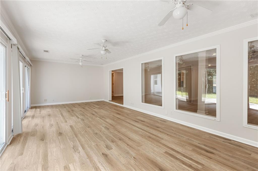 Empty sunroom with light wood-look floors, large windows, and ceiling fans.