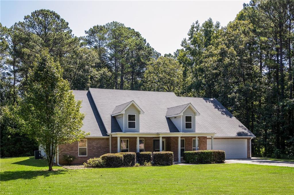 Brick house with two roof dormers and an attached garage, surrounded by a lawn and mature trees.