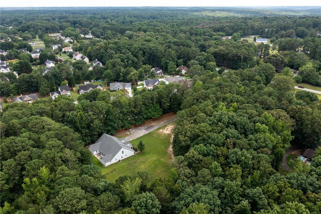 Aerial view of a white house on a grassy, wooded lot near a suburban neighborhood.