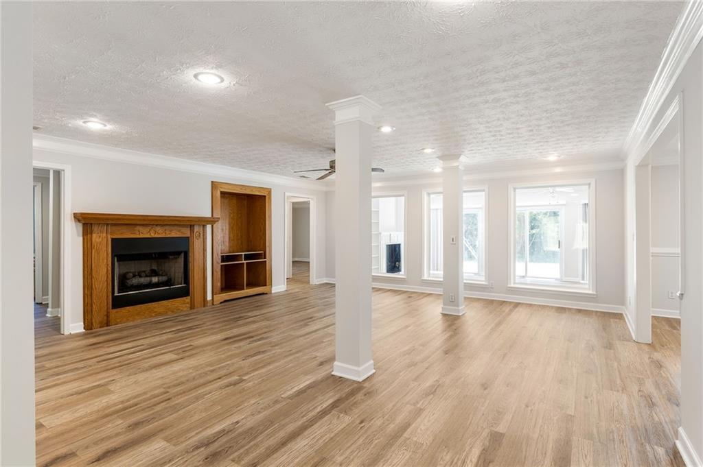 Vacant living room with light wood floors, white columns, and a wood fireplace surround.