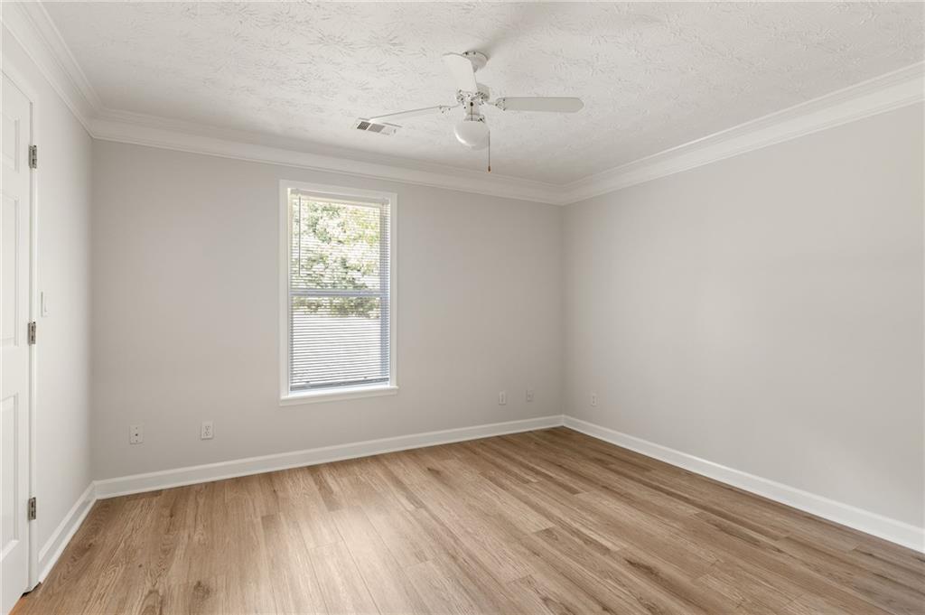 Empty bedroom with wood-look flooring, a window with blinds, and a white ceiling fan.