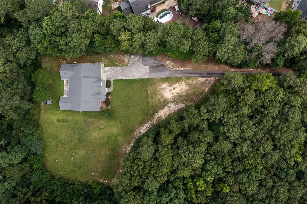 Aerial view of a home surrounded by trees, with a broad lawn and long driveway.
