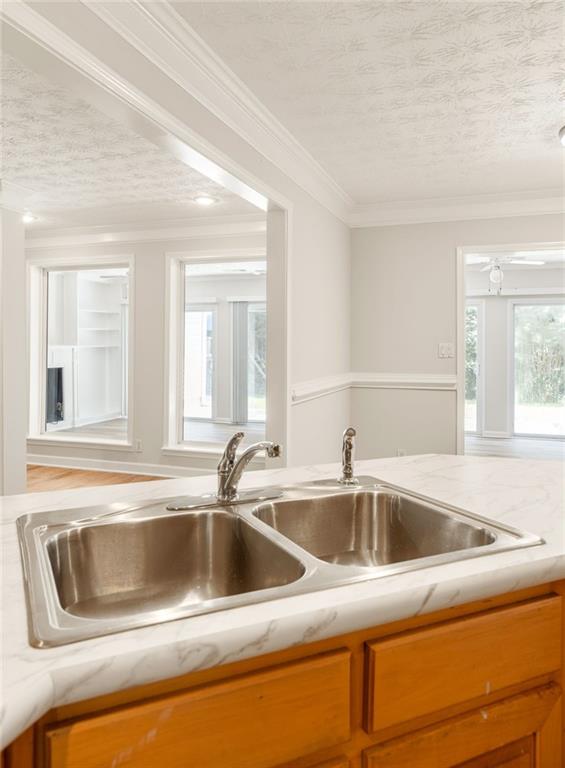 Double-basin kitchen sink in a white marble-look counter above warm wood cabinets.