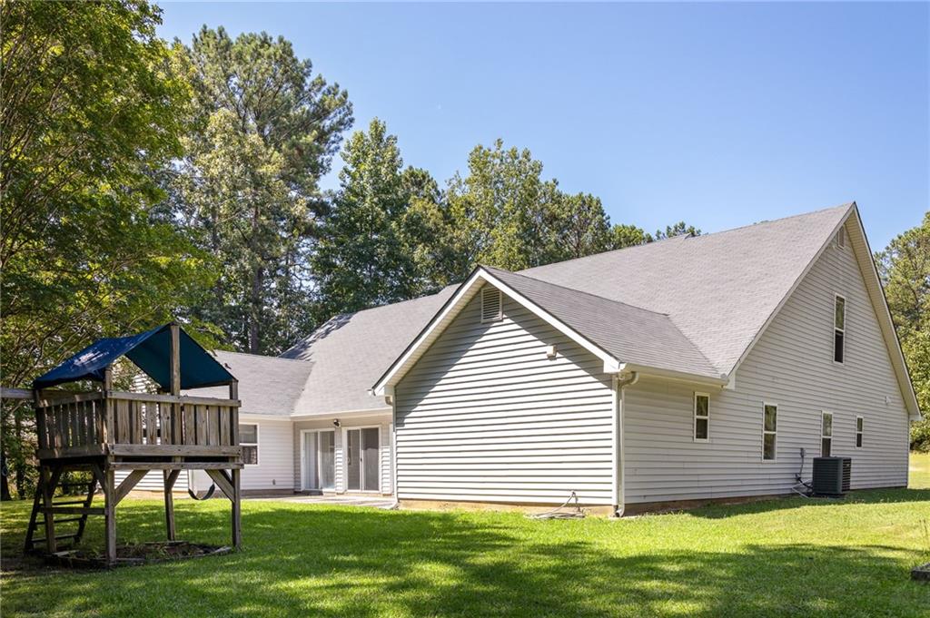 House’s rear and side exterior with a raised wooden play structure, lawn, and trees.
