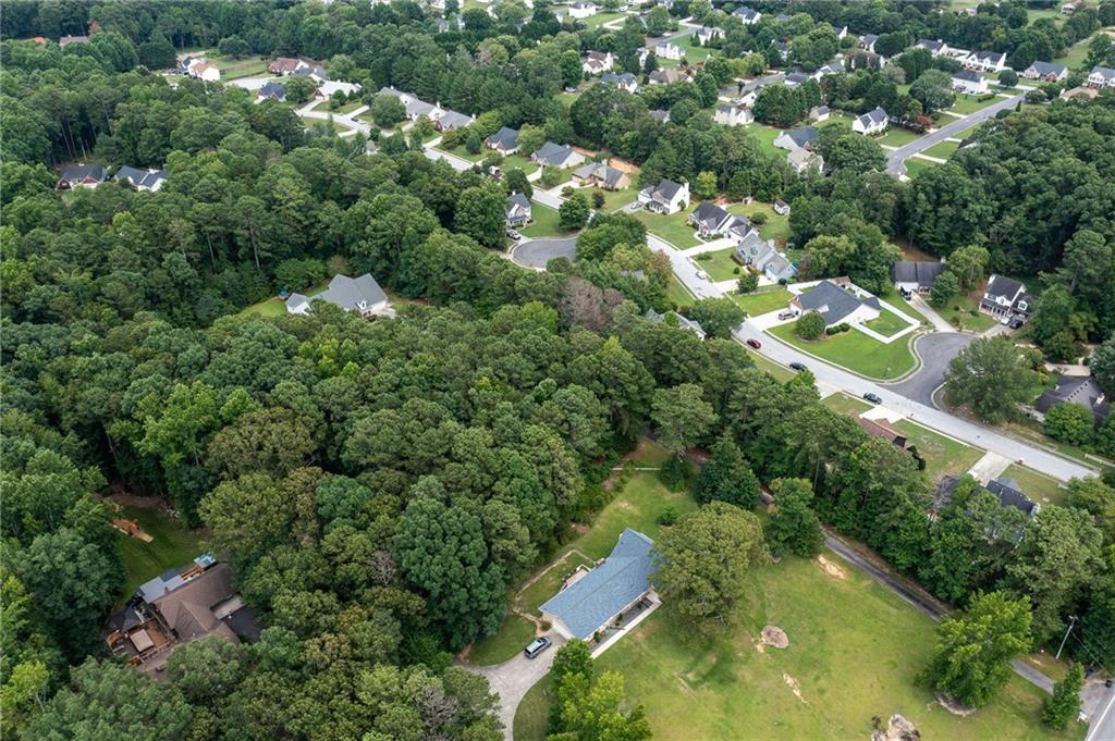 Aerial view of a wooded property beside a neighborhood, with a house and open lawn.