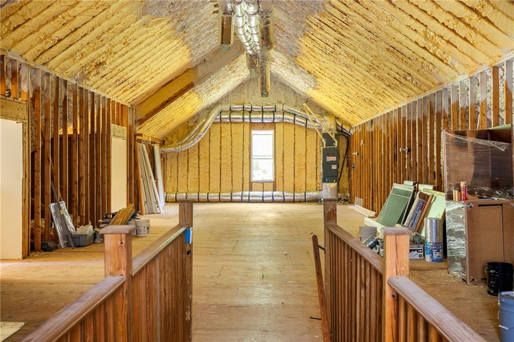 Unfinished attic with exposed insulation, overhead ductwork, and a central walkway.