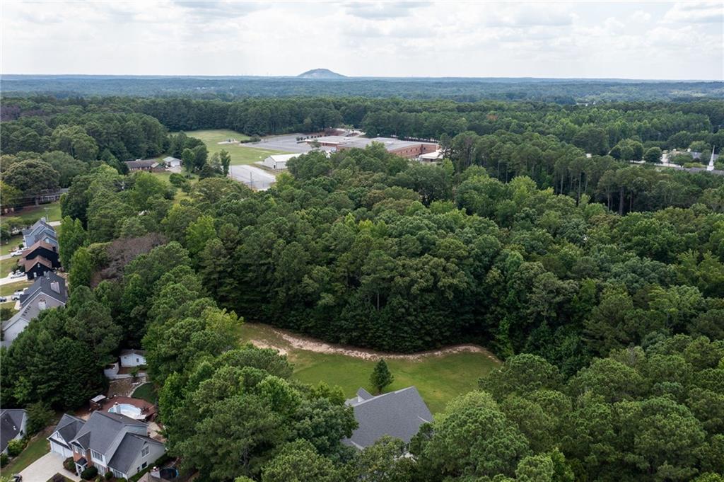Aerial view of wooded property with a grassy clearing, dirt track, and nearby homes.