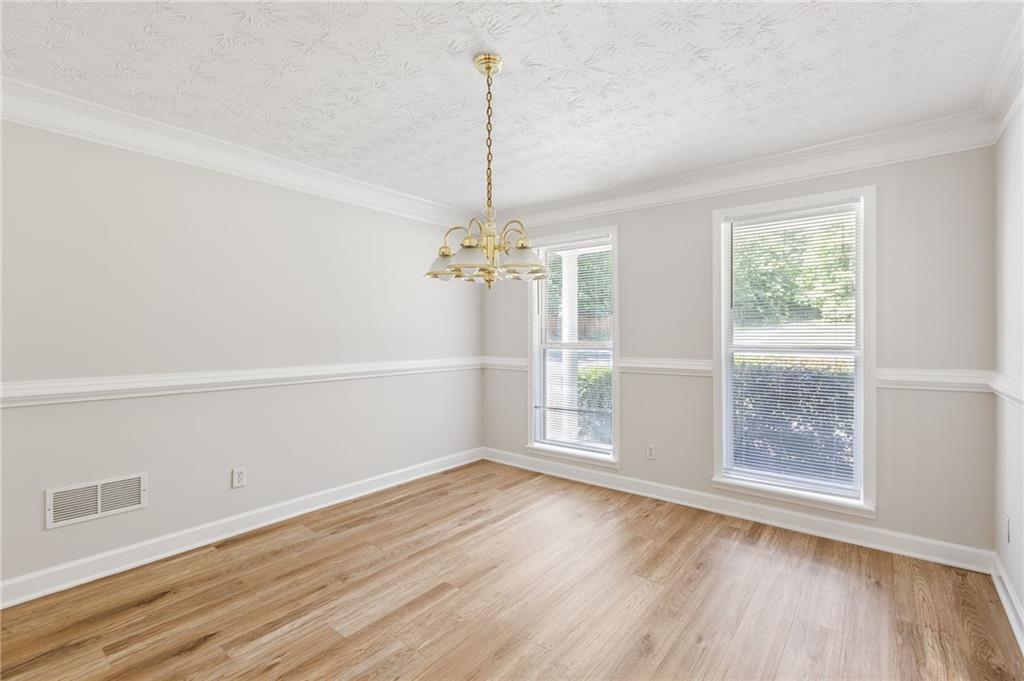 Empty dining room with light wood floors, two windows, and a brass chandelier.