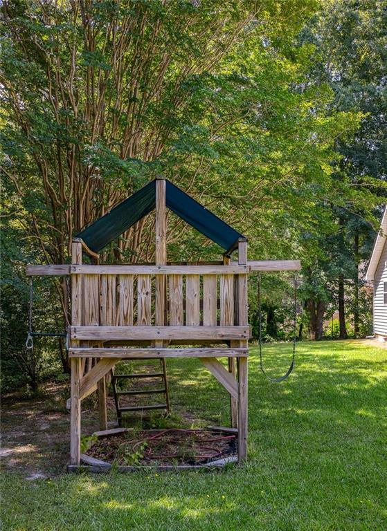 Wooden backyard playset with a blue peaked roof, ladder and swings beneath mature trees.